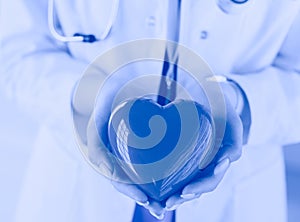 Female doctor with stethoscope holding heart, on light background