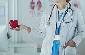 Female doctor with stethoscope holding heart, on light background