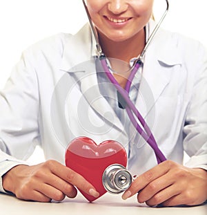 Female doctor with stethoscope holding heart, on light background