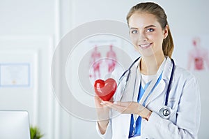 Female doctor with stethoscope holding heart, on light background