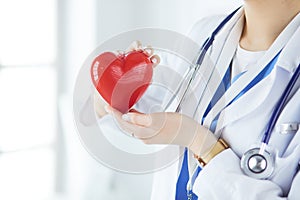 Female doctor with stethoscope holding heart, on light background