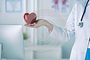 Female doctor with stethoscope holding heart, on light background