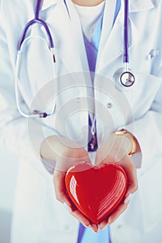 Female doctor with stethoscope holding heart, on light background