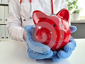 Female doctor with stethoscope holds piggy bank