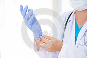 Female doctor with a stethoscope on one shoulder putting on sterile gloves.
