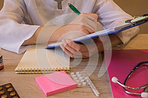 Female doctor with stethoscope sitting at a desk, writing something, prescription or recommendation of the patient