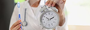 Female doctor stomatologist holding toothbrush and alarm clock in hands