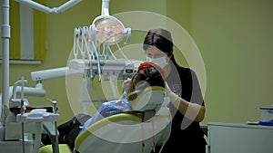 Female doctor stomatologist at work treats and whitens teeth to young woman patient in medical dental clinic