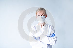 Female doctor surgeon in white uniform, protective blue gloves putting on medical mask hands clasped over grey