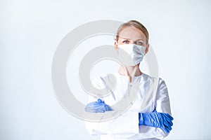 Female doctor surgeon in white uniform, protective blue gloves putting on medical mask hands clasped over grey