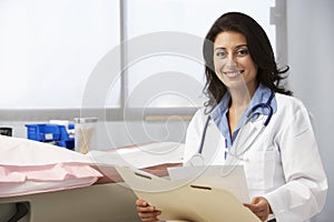 Female Doctor In Surgery Reading Patient Notes