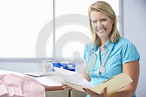 Female Doctor In Surgery Reading Patient Notes