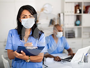 Female doctor in surgical mask filling out medical form
