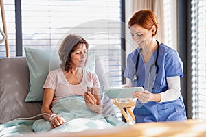 A female doctor with tablet talking to patient in bed in hospital.