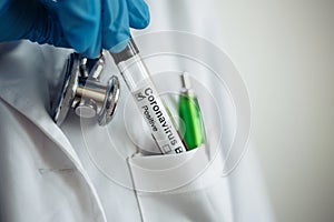 Female doctor takes off the coronavirus blood test tube from her white medical gown pocket. Stethoscope and a green pen. Nurse photo