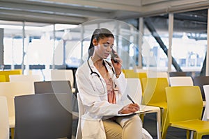 Female doctor talking on mobile phone while writing on a clipboard