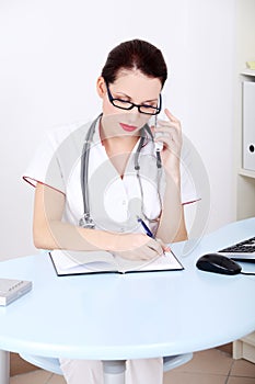 Female doctor talking by the phone and writing.