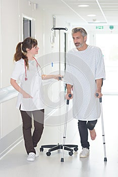 Female doctor talking to male patient with crutches in hospital-corridor