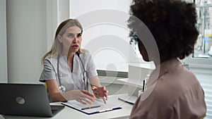 Female doctor talking to patient and sitting at table during working day in clinic spbd.