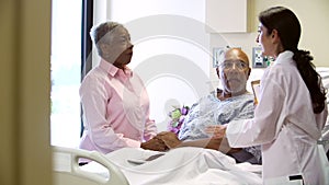 Female Doctor Talking To Senior Couple In Hospital Room