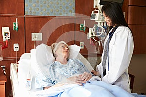 Female Doctor Talks To Senior Female Patient In Hospital Bed
