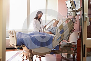 Female Doctor Talks To Senior Female Patient In Hospital Bed