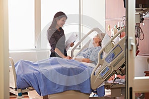 Female Doctor Talks To Senior Female Patient In Hospital Bed