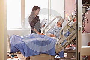 Female Doctor Talks To Senior Female Patient In Hospital Bed