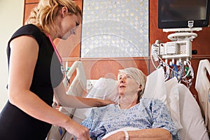 Female Doctor Talks To Senior Female Patient In Hospital Bed