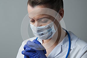 A female doctor therapist in a white robe, mask and gloves. Face close-up. The doctor cries and prays. Tears in eyes