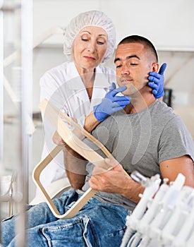 Female doctor, together with male patient, examines face in mirror after undergoing hardware procedure for skin