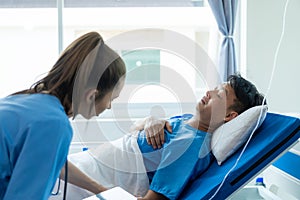 Female doctor treating young male patient in bed and talking with Asian male patient beside bed