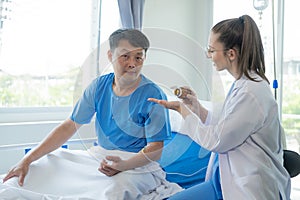 Female doctor treating young male patient in bed and talking with Asian male patient beside bed