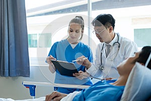 A female doctor and two male doctors treat a young male patient in bed and are talking