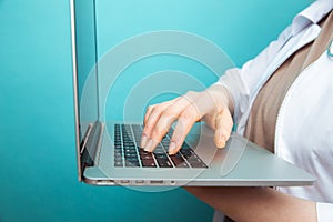 Female doctor in uniform working on laptop computer by keaboard  over blue background. Online medical technology