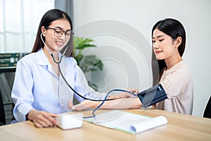 A female doctor using digital sphygmomanometer and stethoscope to check patient's heartbeat at hospital. Medical and health