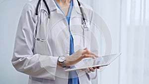 Female doctor using digital tablet in clinic. Healthcare professional with a stethoscope around her neck operating a