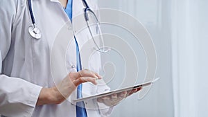 Female doctor using digital tablet in clinic. Healthcare professional with a stethoscope around her neck operating a