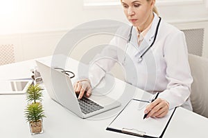 Female doctor using laptop and writing notes