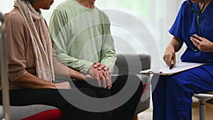 Female doctor using stethoscope examining senior male during home care visit. Elderly healthcare concept