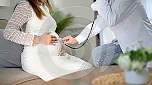 Female doctor using a stethoscope to listen to the baby`s heartbeat in a pregnant woman`s belly