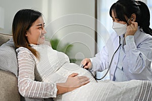 Female doctor using a stethoscope to listen to the baby`s heartbeat in a pregnant woman`s belly