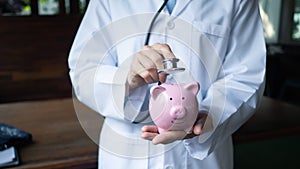 Female doctor is using stethoscope to piggy bank, saving protection concept