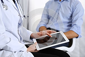 Female doctor using touchpad or tablet computer while consulting man patient in hospital. Medicine and healthcare
