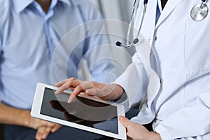 Female doctor using touchpad or tablet computer while consulting man patient in hospital. Medicine and healthcare