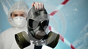 Female doctor virologist in a protection suit and respirator holds a gas mask. Health fight against Coronavirus