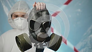 Female doctor virologist in a protection suit and respirator holds a gas mask. Health fight against Coronavirus