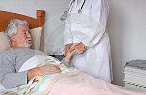 Female doctor visiting a senior patient at home checking temperature. Elderly man worried lying in bed