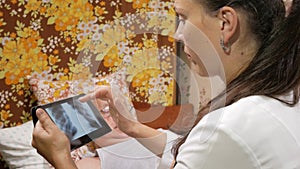 A female doctor visits a patient at home. It shows the results of the X-ray on a tablet computer. The man is lying on