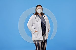 Female doctor wearing a protective face mask with hands on pocket of white coat looking at camera